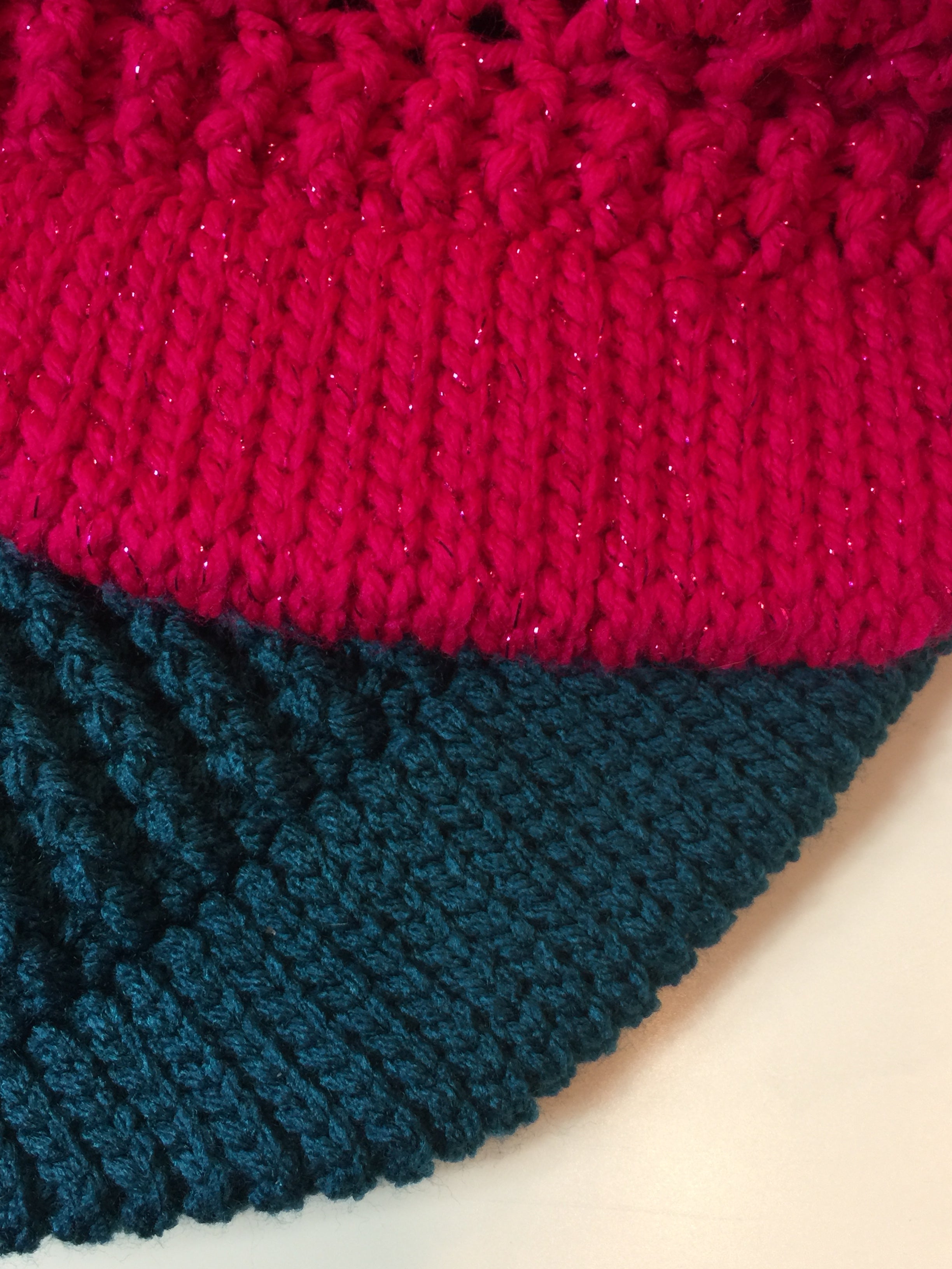 Close-up of two knitted fabrics: one in bright pink with a textured pattern, perfect for creating a stylish “messy bun” hat, and the other in dark green with a ribbed design inspired by the classic look of the Ribbed for Him & Her Crochet Hat Pattern PDF, both displayed on a light surface.