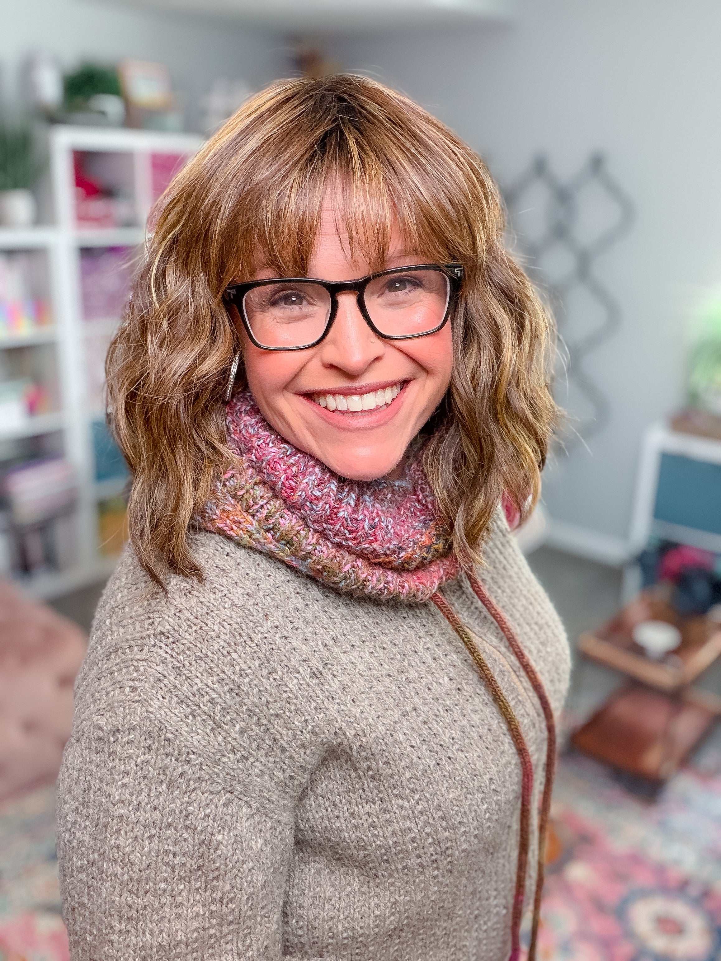 A smiling woman wearing glasses and a multicolored Cozy Sideline Knit Balaclava - PDF.