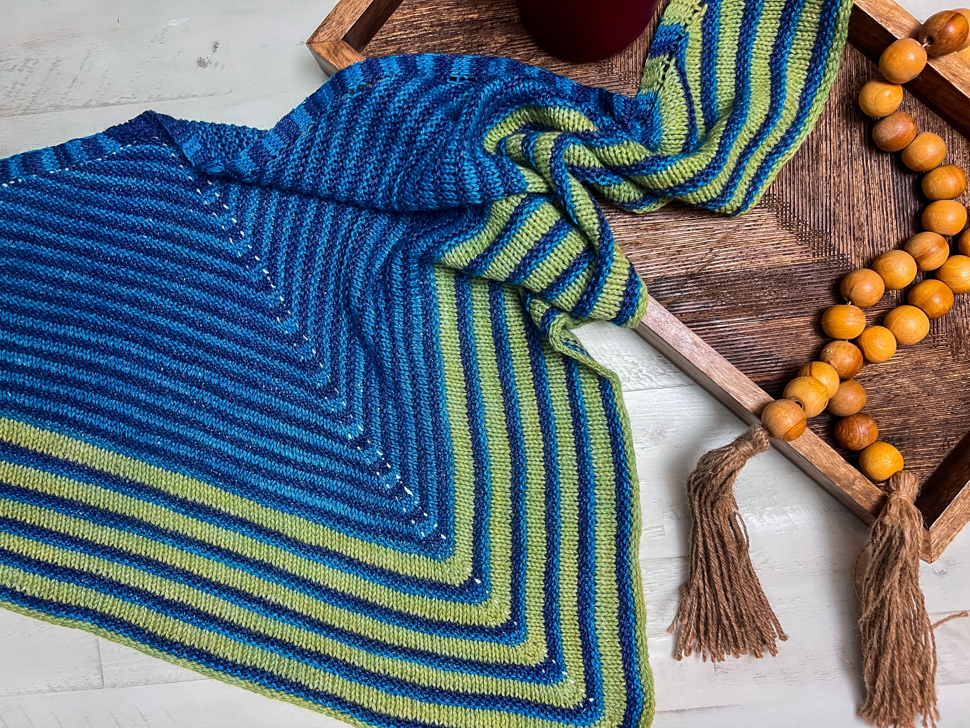 Blue and green striped fabric with tassels on a wooden tray. Make It Mine Knit Shawl triangle shawl pattern garter stitch striped knit wrap 