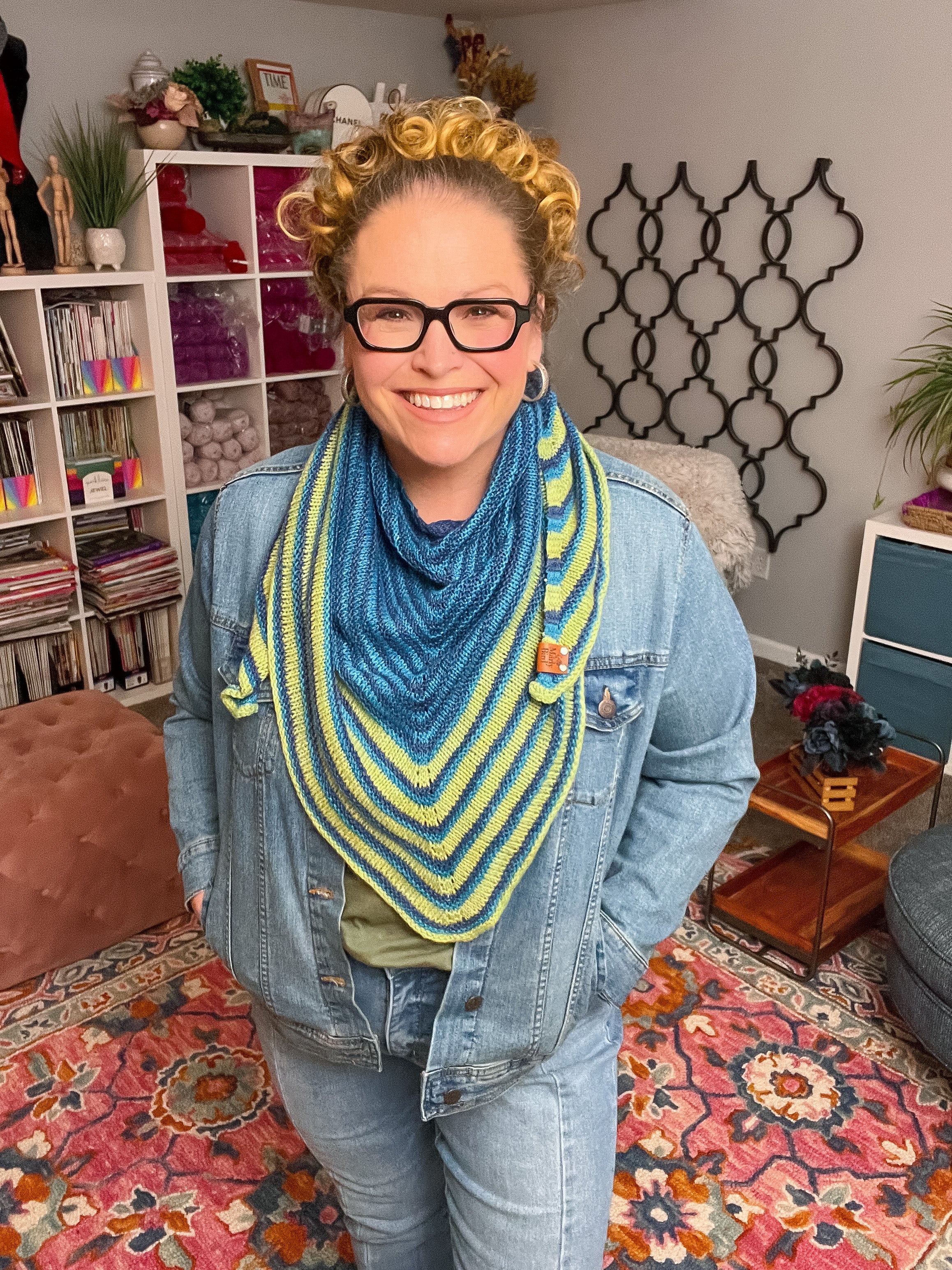 Person wearing a blue and yellow knitted scarf in a cozy living room. Make It Mine Knit Shawl triangle shawl pattern garter stitch striped knit wrap