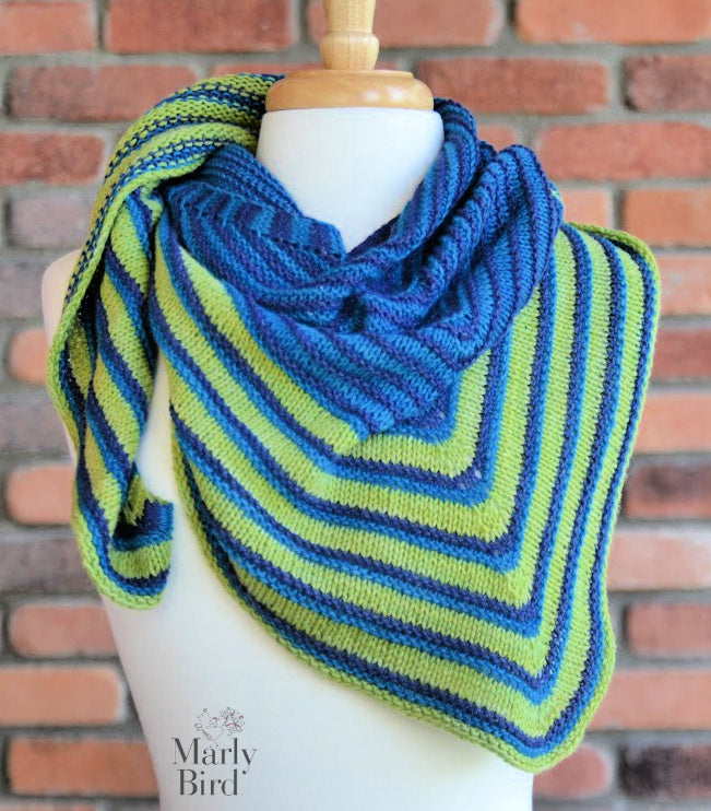 Mannequin wearing a blue and green striped knitted shawl with 'Marly Bird' branding against a brick wall. Make It Mine Knit Shawl triangle shawl pattern garter stitch striped knit wrap