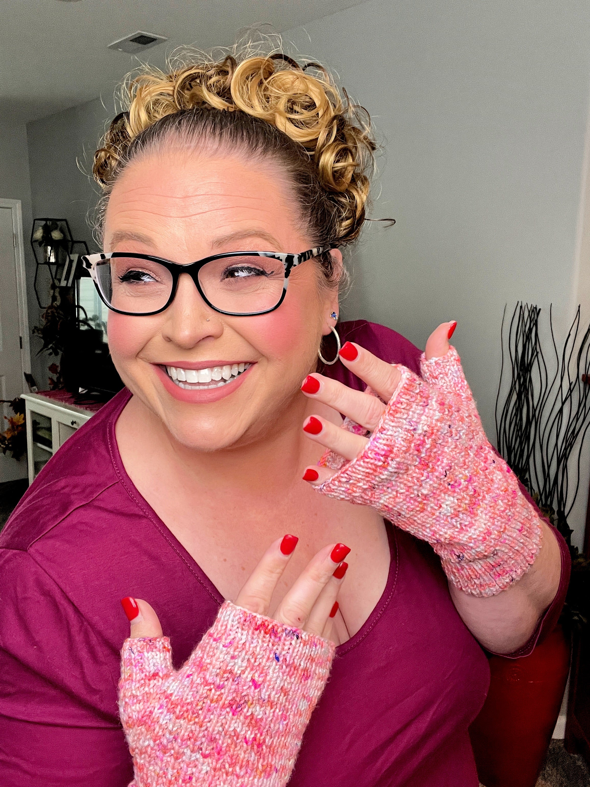 Model in a magenta top wearing pink speckled fingerless mittens with open fingertips and ribbed cuffs.