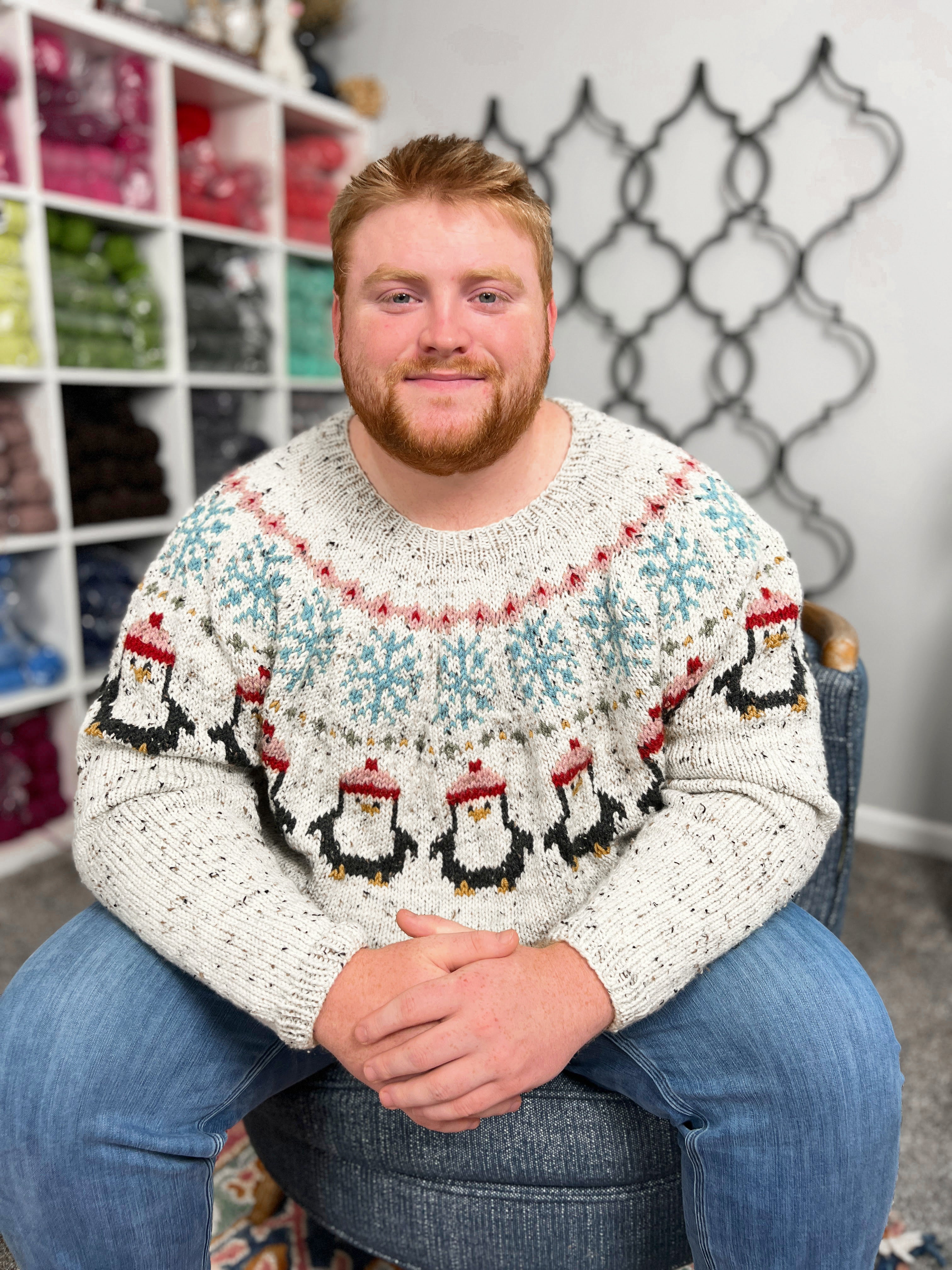 Man wearing a patterned sweater sitting on a chair with a decorative wall in the background