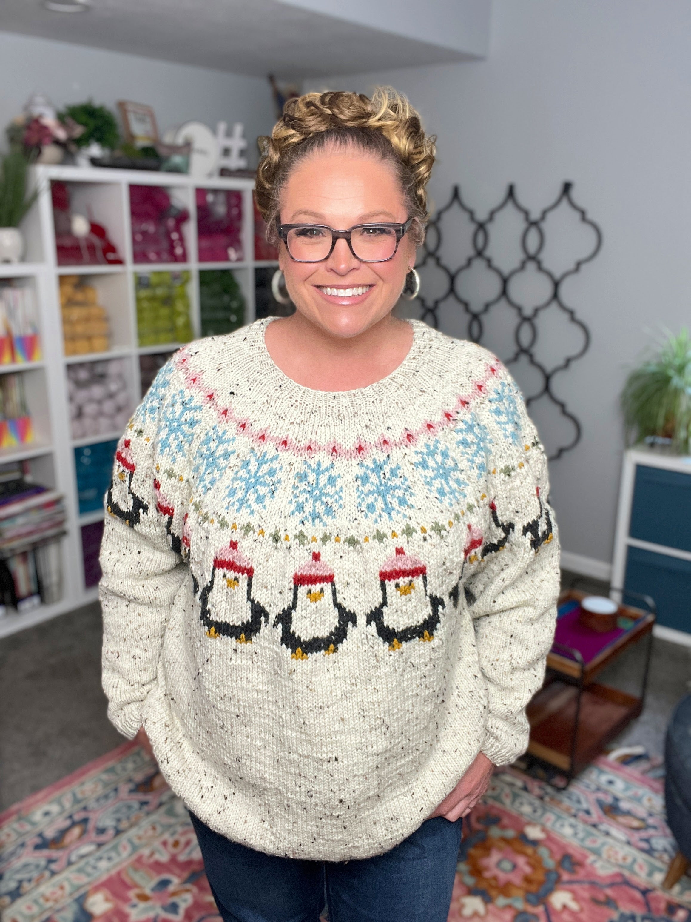 Person wearing a sweater with penguin design in a room with shelves and decor.