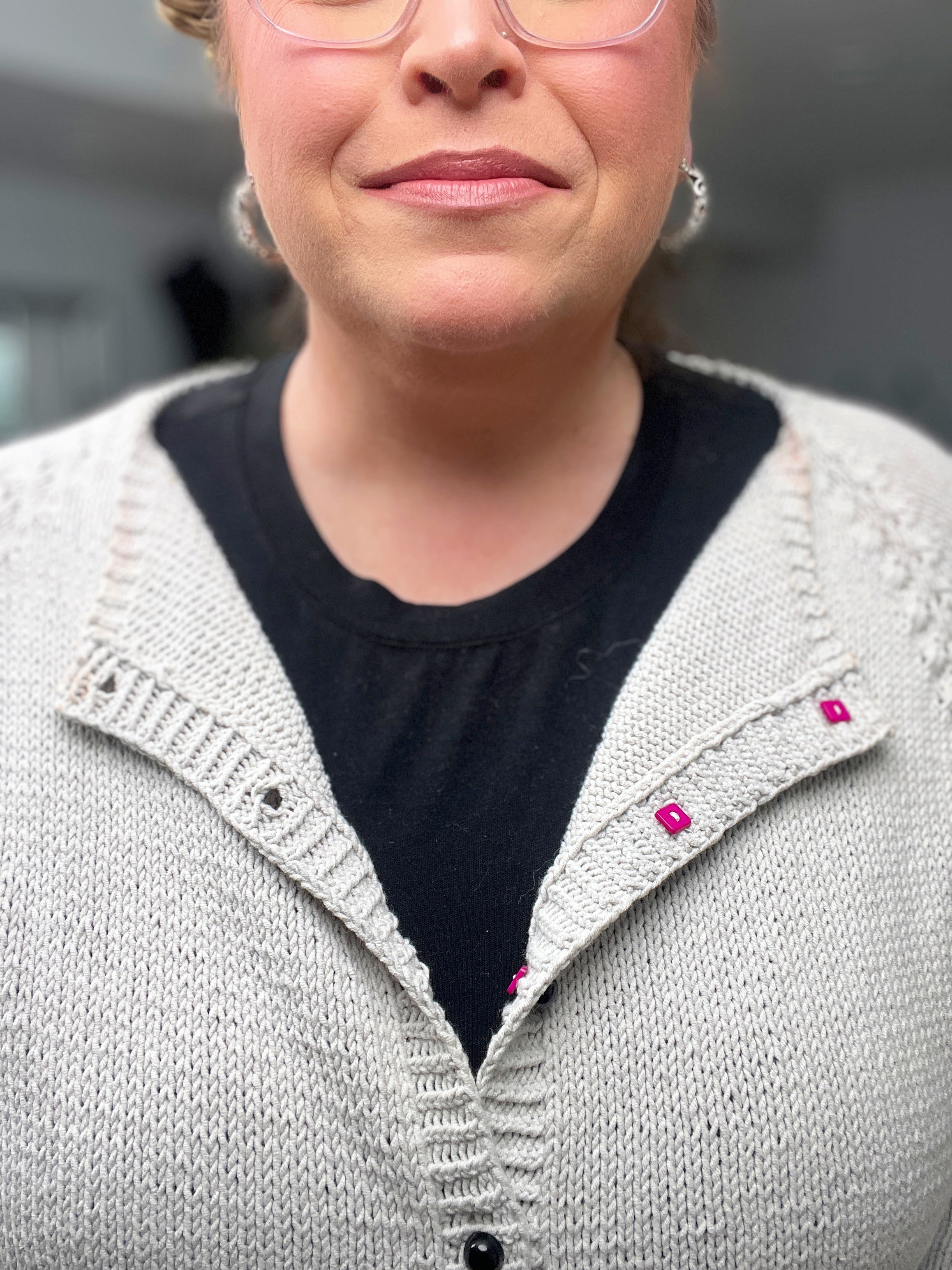 Person wearing a gray knitted cardigan with pink buttons on a blurred background