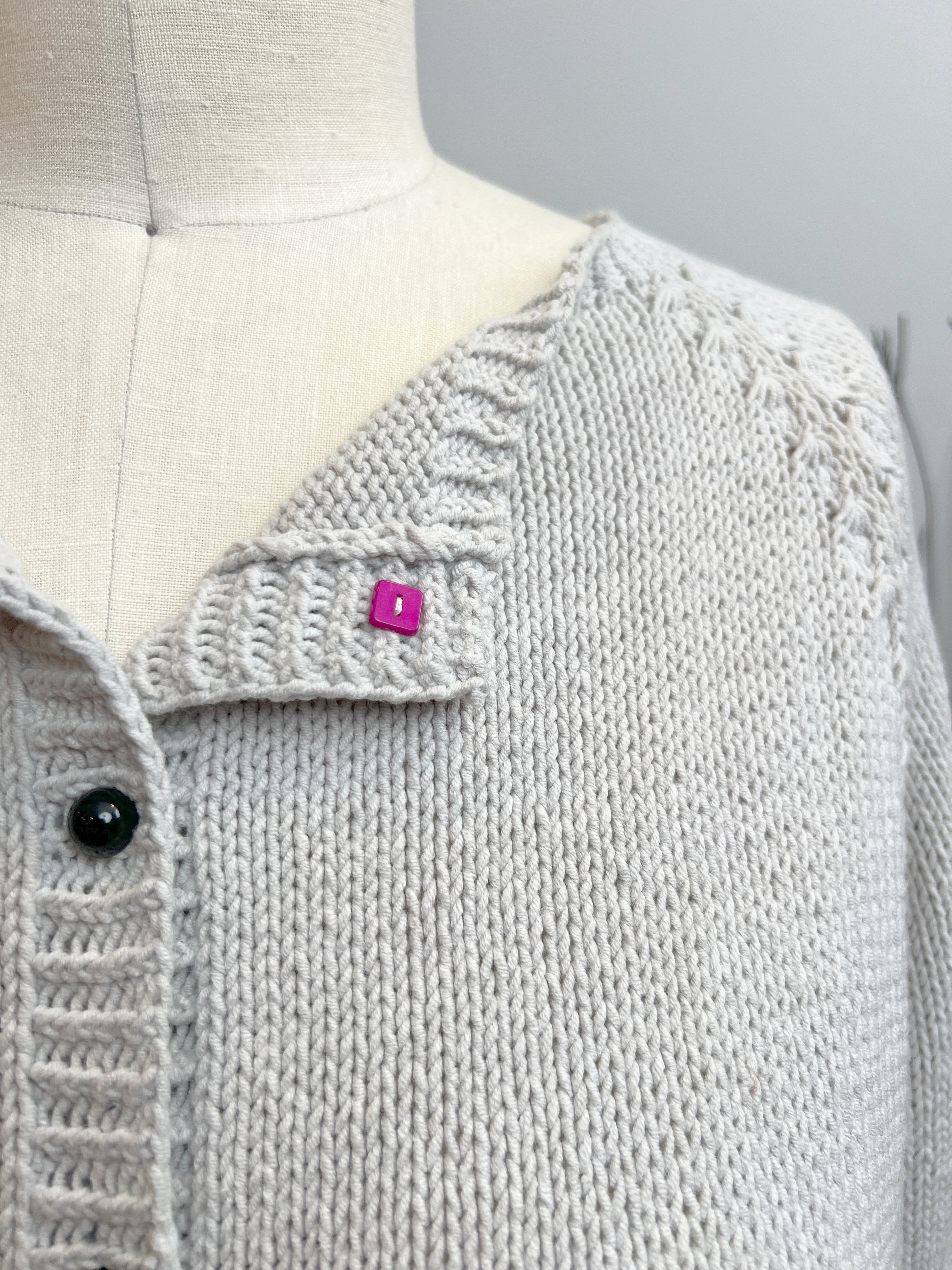 Gray knitted cardigan on a mannequin with a pink tag, against a plain background