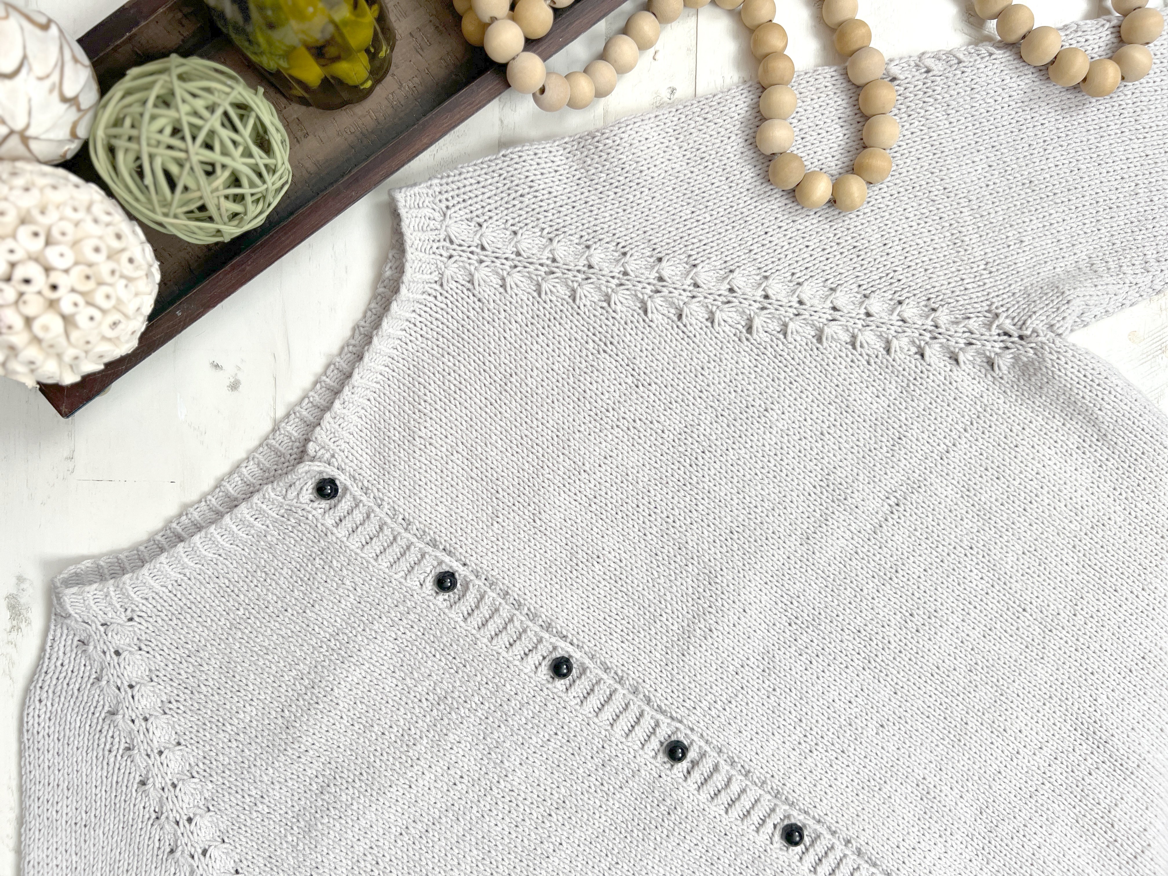 Gray sleeveless top with button details on a white surface with decorative items.