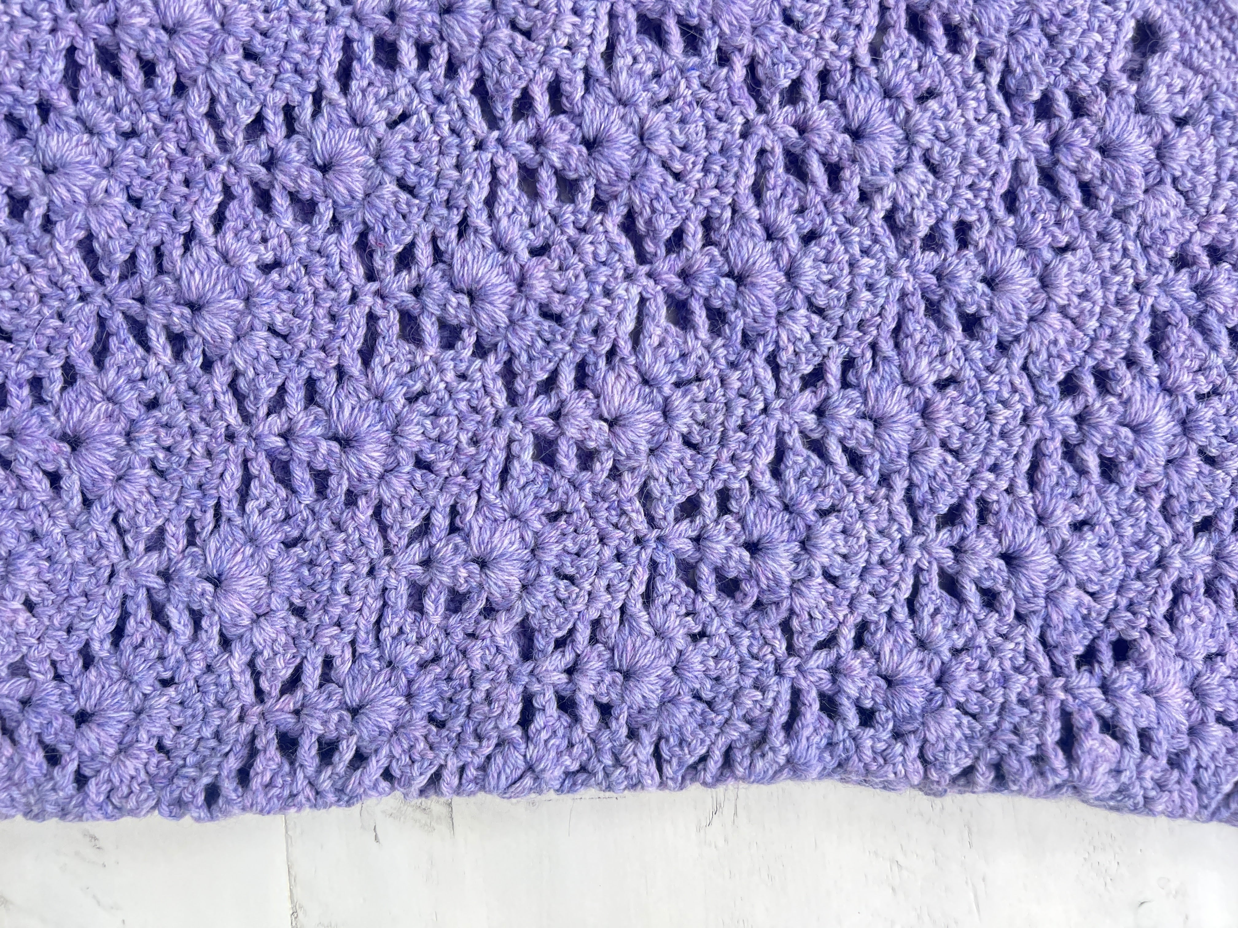 Close-up of a lavender crocheted fabric with a textured, floral-like pattern, displayed on a light-colored surface—perfect inspiration for a lace stitch crochet sweater or the Tatiana Crochet Lace Tunic – Lace Crochet Top PDF (Sizes S–2X).