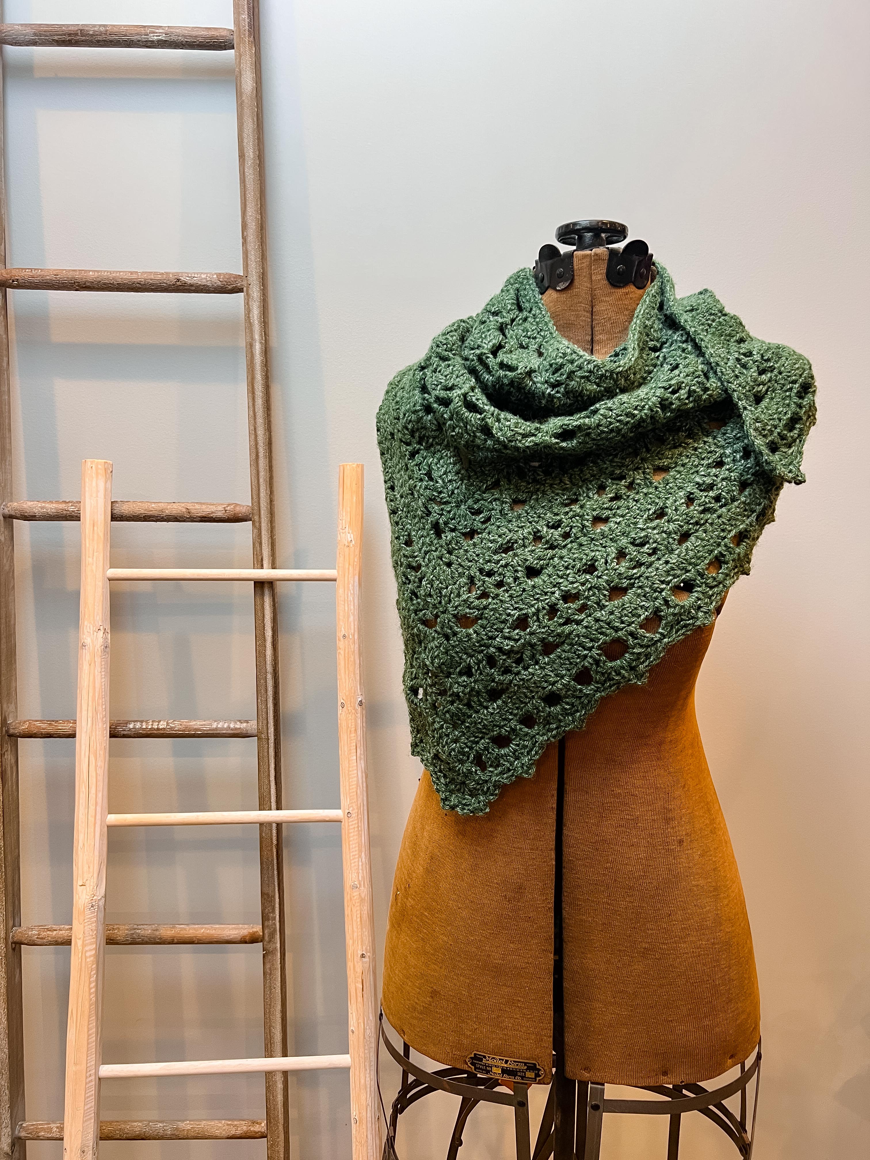Green crocheted shawl on a mannequin with a wooden ladder in the background