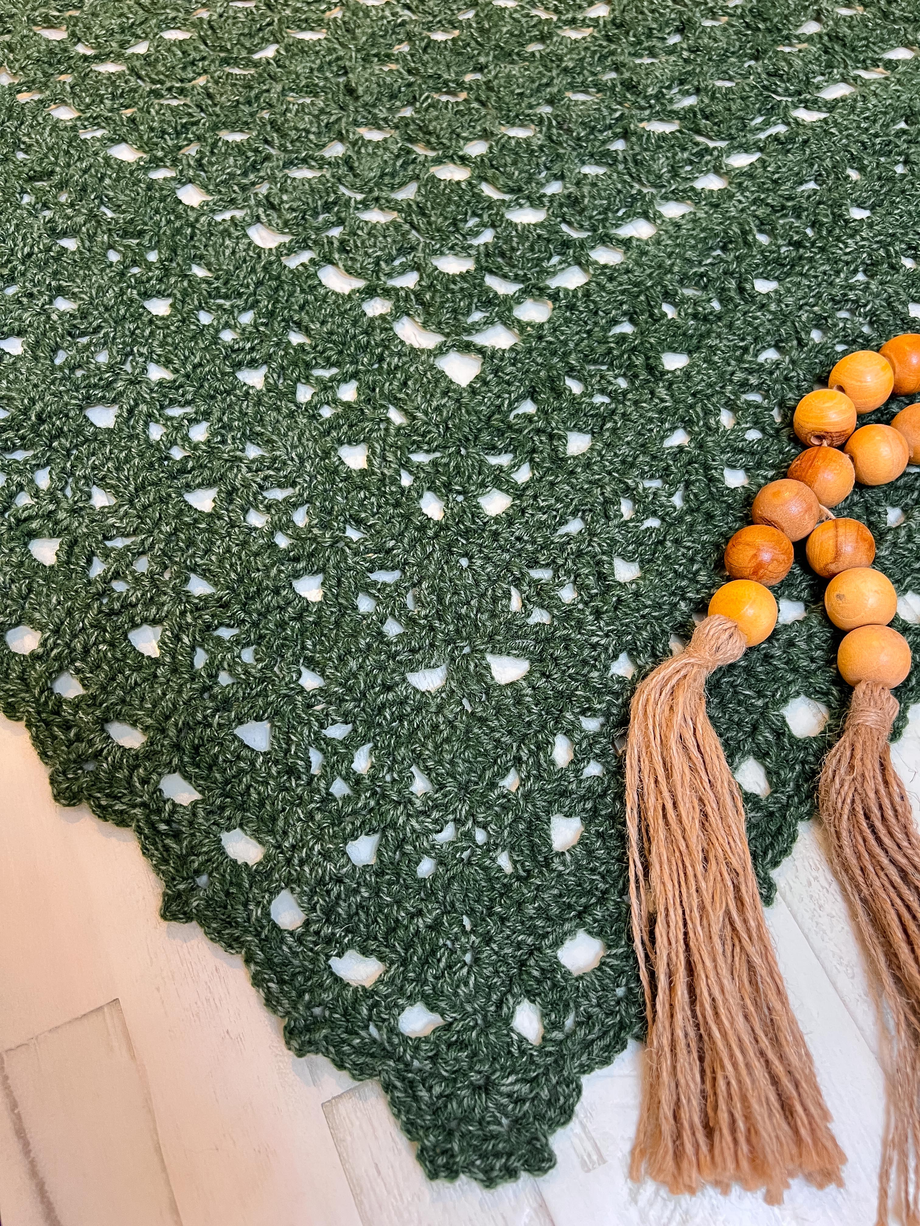 Green crocheted shawl with white accents and orange beads with tassels on a wooden surface.